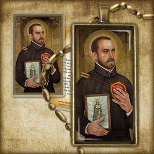May include: A religious pendant featuring a colorful image of Saint Roque, a Catholic saint, holding a heart pierced by an arrow. The pendant is framed in a silver-toned metal and has a detailed design.