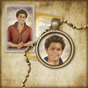 May include: A gold-toned pendant necklace with a round glass charm featuring a portrait of a young man with brown hair and a light blue shirt. The charm is surrounded by a gold-toned metal frame. The necklace is made of gold-toned metal beads.