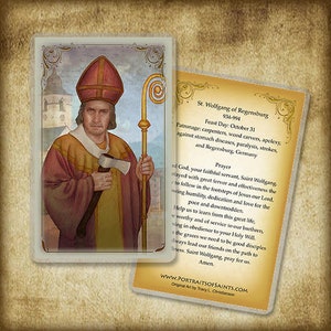 May include: A religious card featuring a portrait of St. Wolfgang holding an axe and a staff. The saint is dressed in traditional robes and a red hat. A second card with text about St. Wolfgang is visible.