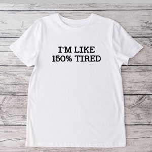 K&ouml;nnte beinhalten: Wei&szlig;es T-Shirt mit schwarzem Text, der "Ich bin wie 150% m&uuml;de" lautet.