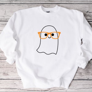 May include: White sweatshirt with a cartoon ghost wearing orange glasses. The ghost has a smiling face.