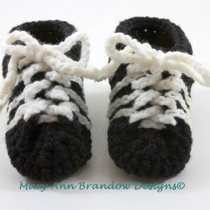 May include: A pair of black and white crocheted baby booties with white laces. The booties are tied in a bow at the top.