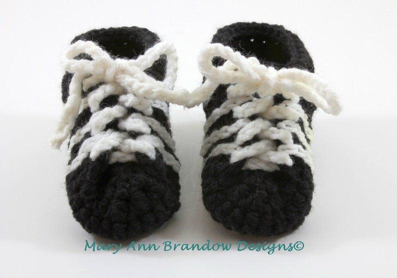 May include: A pair of black and white crocheted baby booties with white laces. The booties are tied in a bow at the top.