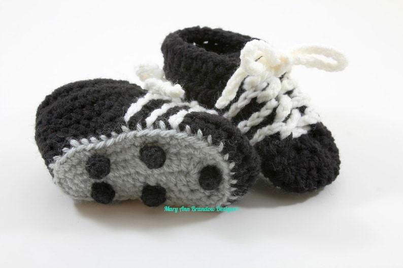 May include: A pair of black and white crocheted baby booties with gray soles that resemble soccer cleats.