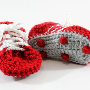 May include: A pair of red and gray crocheted baby booties with white laces. The booties have a textured sole with small red circles.