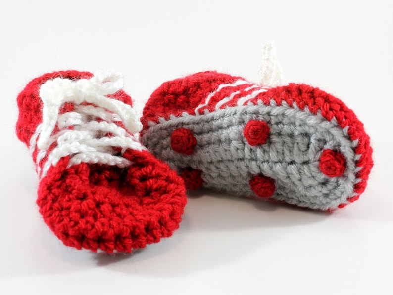 May include: A pair of red and gray crocheted baby booties with white laces. The booties have a textured sole with small red circles.