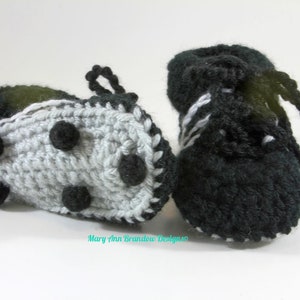 May include: A pair of crocheted baby booties in black and white. One bootie has a black and white striped design, while the other has a gray base with black dots and a black trim.