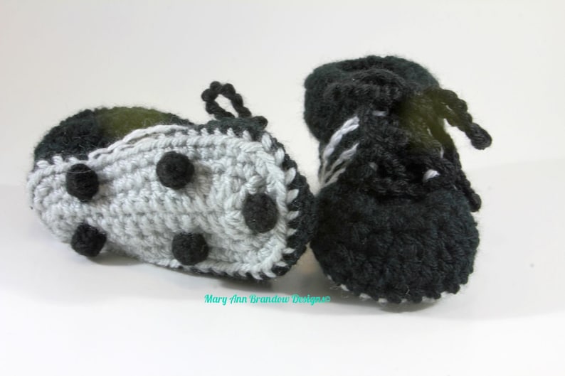 May include: A pair of crocheted baby booties in black and white. One bootie has a black and white striped design, while the other has a gray base with black dots and a black trim.