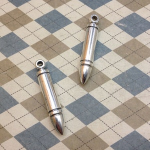 May include: Two silver bullet-shaped charms with a loop at the top for attaching to a necklace or bracelet.