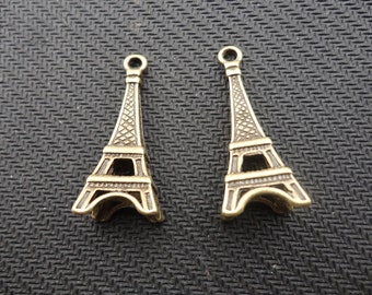 Peut inclure: Deux breloques en métal de couleur dorée en forme de Tour Eiffel. Les breloques sont détaillées et ont une boucle en haut pour être attachées à des bijoux ou d'autres objets artisanaux.