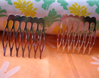 May include: Two silver-colored hair combs with curved teeth. The combs have a scalloped top edge and are set against a peach-colored surface with a floral pattern in the background. The combs are designed to be inserted into the hair.