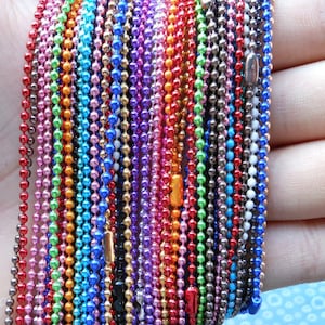 May include: A selection of colourful metal chain necklaces, each with a different colour and finish. The chains are arranged in a row, with the ends of the chains hanging down. The chains are all the same length.