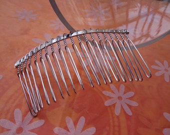May include: A silver-colored hair comb with a series of long, thin tines. The comb's top section features a twisted wire design. The comb is set against an orange background with a floral pattern, creating a contrast of textures and colors.
