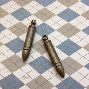 Puede incluir: Dos abalorios de color dorado antiguo en forma de bala con un bucle en la parte superior para sujetarlos a un collar o pulsera.