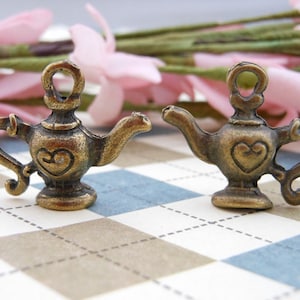 May include: Two antique gold-toned teapot charms with heart details. The charms are perfect for adding a vintage touch to jewelry or crafts.