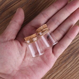 Puede incluir: Dos pequeñas botellas de vidrio transparente con tapones de corcho. Las botellas están vacías y tienen forma redonda.