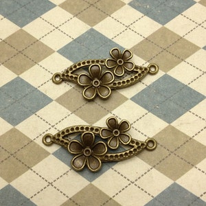 May include: Two antique gold-toned metal flower charms with a decorative design. Each charm features two stylized flowers with a beaded border.