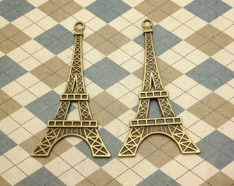 Puede incluir: Dos encantos de metal dorado en forma de Torre Eiffel. Los encantos están sobre un fondo a cuadros marrón y azul.