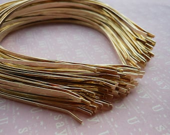 May include: A stack of gold-colored metal headbands. The headbands are all the same size and shape, and they are arranged in a neat pile.