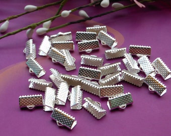 May include: A pile of silver-toned metal clasps for jewelry making. The clasps are rectangular with a textured surface and have a small loop on each end.