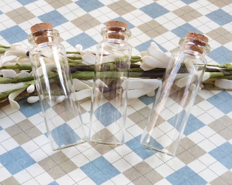 Puede incluir: Tres botellas de vidrio transparente con tapones de corcho. Las botellas están de pie sobre una superficie a cuadros.