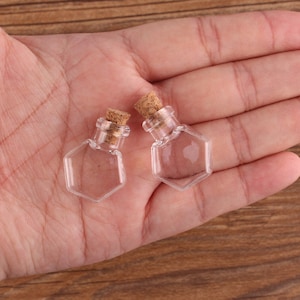 May include: Two small, clear glass bottles with cork stoppers. The bottles are hexagonal in shape and have a smooth, polished finish.