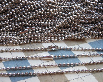 May include: A close-up of a silver ball chain, with multiple strands of the chain lying on a checkered surface. The chain is made of small, round metal beads.