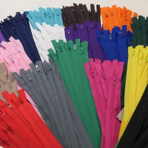 以下が含まれることがあります： 赤、ピンク、紫、青、緑、黄色、黒など、さまざまな色合いのカラフルなファスナーのコレクション。 ファスナーは扇状に配置され、さまざまな色とスタイルが示されています。 縫製や手芸プロジェクト用です。