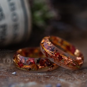 Puede incluir: Dos anillos de resina con flores secas y pan de oro incrustados. Los anillos son transparentes y tienen una paleta de colores cálida y otoñal.