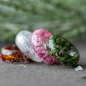 May include: Four resin rings with embedded flowers. The rings are in shades of green, pink, white, and orange.