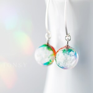 May include: A pair of silver dangle earrings with white and rainbow coloured glass orbs. The orbs have a speckled, cloudy appearance.