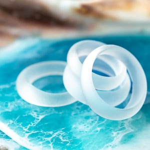May include: A set of four frosted white silicone rings, arranged in a spiral, on a blue and white background.