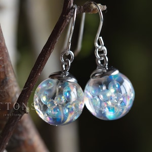 Könnte beinhalten: Ein Paar silberne Ohrhänger mit irisierenden Glaskugeln, die mit kleinen, irisierenden Perlen gefüllt sind.