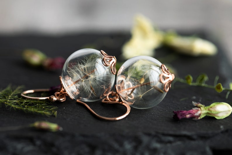 Pode incluir: Um par de brincos de ouro rosa com esferas de vidro transparente que cont&ecirc;m sementes de dente-de-le&atilde;o secas.