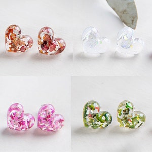 May include: Four pairs of heart-shaped resin earrings with pressed flowers and glitter. The earrings are in four colors: brown, white, pink, and green.