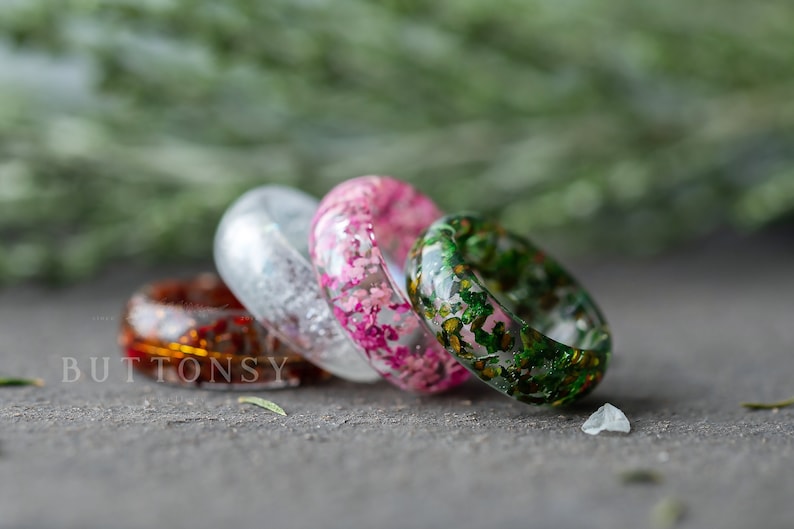 May include: Four resin rings with embedded flowers. The rings are in shades of green, pink, white, and orange.