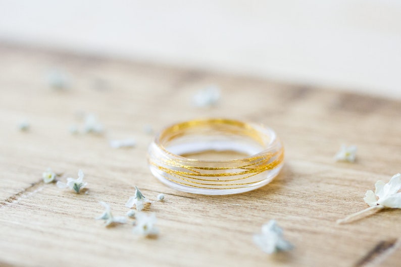 May include: A clear resin ring with thin gold wire wrapped around it. The ring is on a wooden surface.
