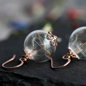 Pode incluir: Um par de brincos de ouro rosa com esferas de vidro transparentes que cont&ecirc;m sementes delicadas de dente-de-le&atilde;o.