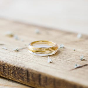 May include: A clear glass ring with gold wire wrapped around it. The ring is sitting on a wooden surface.