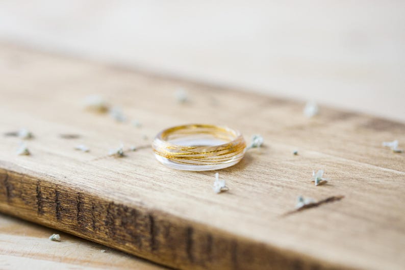 May include: A clear glass ring with gold wire wrapped around it. The ring is sitting on a wooden surface.