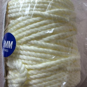 May include: A large spool of cream-colored yarn, tightly wound and encased in clear plastic. The yarn appears thick and textured. A blue sticker indicates the yarn's thickness as 6mm.
