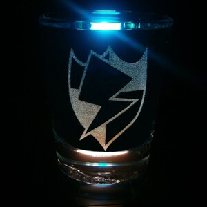 May include: A clear glass shot glass with a black and white lightning bolt design etched into the side.