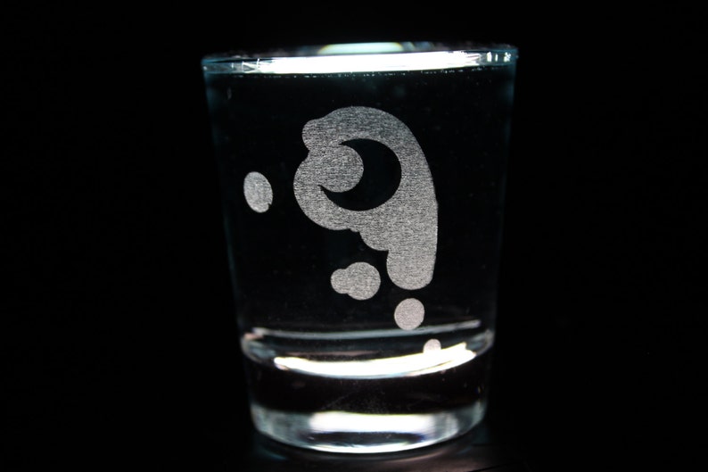 Może przedstawiać: Przezroczysty szklany kieliszek do shot&oacute;w z wygrawerowanym białym wzorem w kształcie p&oacute;łksiężyca i spirali. Szklanka jest wypełniona przezroczystym płynem.