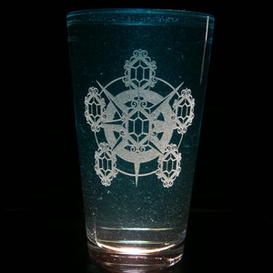 Pode incluir: Um copo transparente com um tom azul esverdeado e um desenho gravado em branco de uma estrela com formas geométricas ao redor.