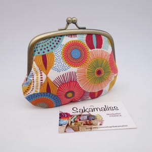May include: A fabric coin purse with a kiss-lock metal clasp featuring a colourful pattern of circles and abstract shapes in shades of red, orange, yellow, and blue. A white rectangular tag with the text Sakamaliss Montpellier FRANCE is included.