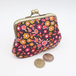 Petit porte-monnaie à fermoir en métal retro, motif fleuri rose et orange sur fond noir, deux sections contrastées pour cartes et espèces