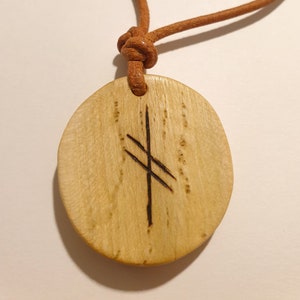 Könnte beinhalten: Ein Holzanhänger mit einer braunen Lederschnur. Der Anhänger ist rund und hat ein eingebranntes Symbol, das aus einer vertikalen Linie mit zwei horizontalen Linien besteht, die sie kreuzen.