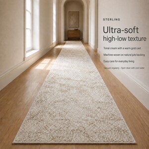 May include: A long runner rug with an ultra-soft high-low texture in a tonal cream color with a warm gold cast. The rug features a machine-woven construction on a natural jute backing. Text on the image reads: STERLING, Ultra-soft high-low texture.