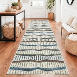 May include: A long, rectangular rug with a cream-colored background and a repeating pattern of horizontal stripes in shades of blue, brown, and green. The rug is placed in a hallway with wooden flooring and a white door.