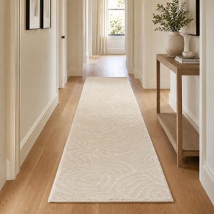 May include: A long, rectangular runner rug in a neutral cream color, featuring a subtle, tone-on-tone embossed pattern of swirling, circular lines that create a textured appearance across the entire surface of the floor covering.
